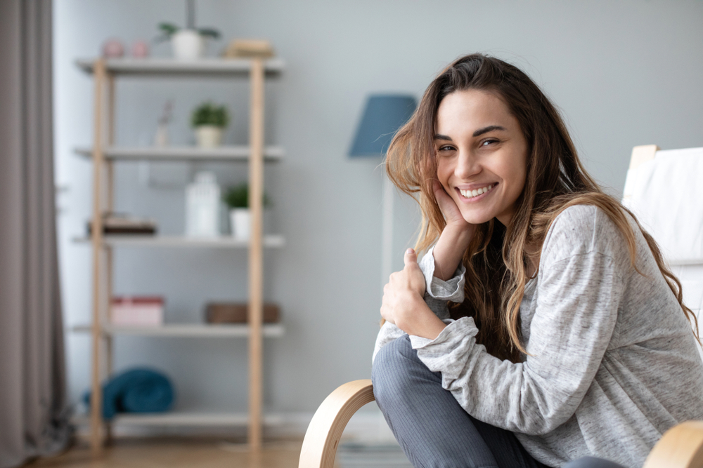 A young woman sitting comfortably at home, smiling with confidence and showing her bright teeth - North Park Dentist.