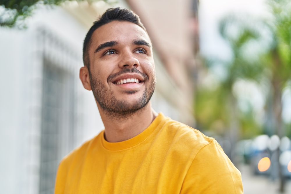 A cheerful young man in a yellow shirt smiling confidently outside, showing his bright teeth - North Park Dentist.